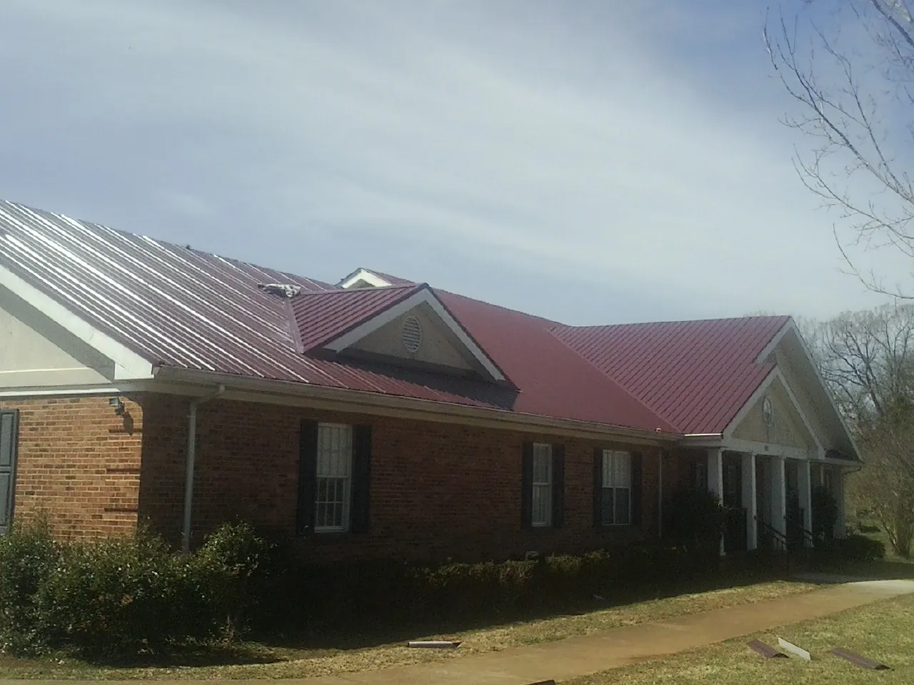 Red metal roof with gabled entries on a long brick building, from a Hail Damage Roof Repair job in Livingston